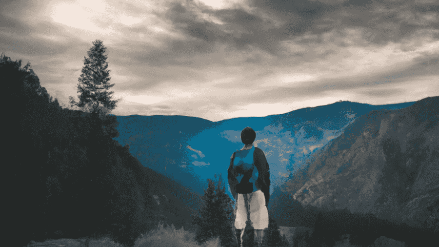 An image of a lone traveler standing on a mountaintop overlooking a breathtaking view.